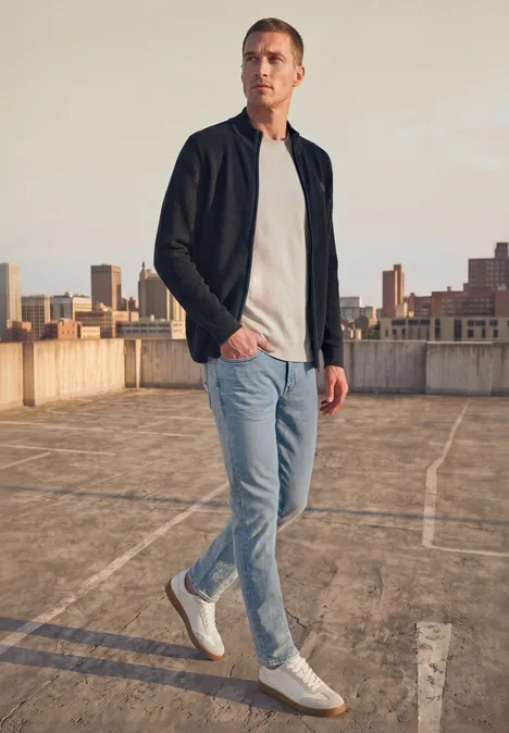 Strickjacke mit Stehkragen und Struktur dark basic blue Ein Mann in Jeans, T-Shirt und Jacke läuft auf einem sonnigen Parkdeck im urbanen Umfeld.