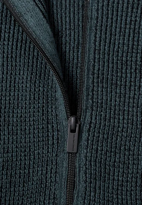 Nahaufnahme eines dunkelgrünen, gerippten Strickpullovers mit Reißverschluss.