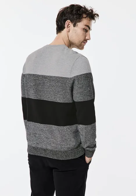 Mann mit grauem und schwarzem Pullover blickt über die Schulter.