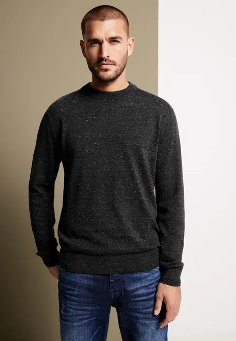 Mann mit dunklem Pullover und Jeans vor geteiltem Hintergrund.