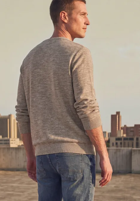 Ein Mann steht auf einem Dach und blickt auf die Stadt, trägt Pullover und Jeans.