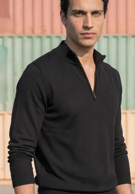 Basic Pullover mit Troyerkragen Black Ein Mann trägt einen schwarzen Pullover mit Reißverschlusskragen vor bunten Containern.