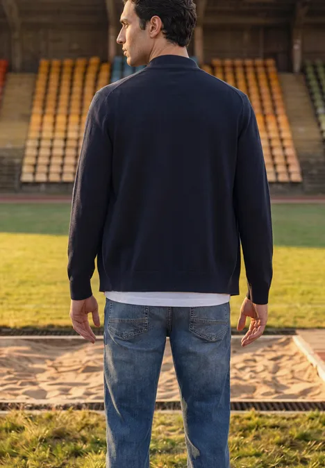 Basic Pullover mit Troyerkragen dark basic blue Ein Mann steht mit dem Rücken zur Kamera in Jeans und Pullover auf einer Bahn mit Sandmulde im Stadion.