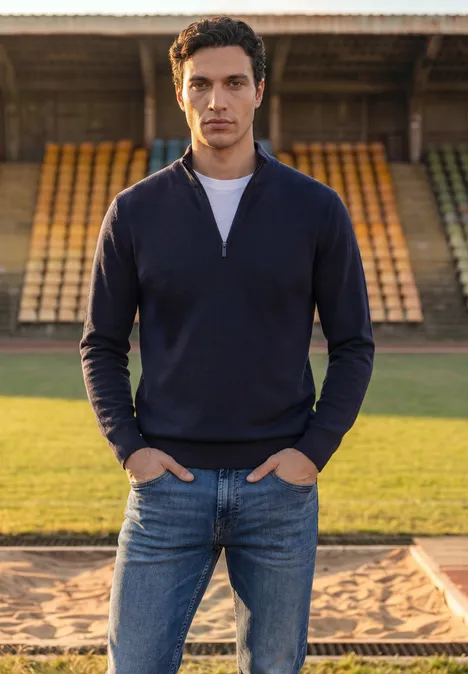 Basic Pullover mit Troyerkragen dark basic blue Ein Mann in Jeans und dunkelblauem Pullover steht vor leeren Zuschauerrängen eines Stadions.