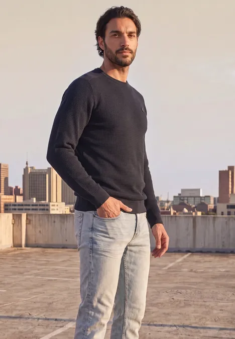 Pullover mit Rundhals und Schulterdetail dark basic blue Ein Mann im schwarzen Pullover und Jeans steht auf einem Dach mit Stadtsilhouette im Hintergrund.