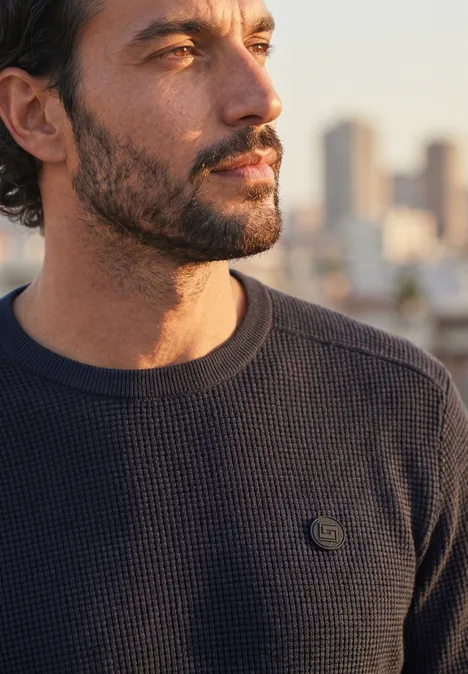 Pullover mit Rundhals und Schulterdetail dark basic blue Ein nachdenklicher Mann mit Bart und dunklem Pullover vor einer verschwommenen Stadtkulisse im Abendlicht.