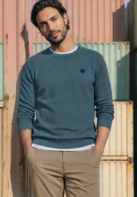 Pullover mit Rundhals und Schulterdetail cold blue Ein Mann in lässigem Pullover und Chinos lehnt vor bunten Containern.