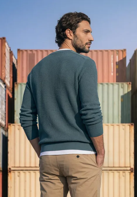 Pullover mit Rundhals und Schulterdetail cold blue Ein Mann in Pullover und Chino steht vor bunten Frachtcontainern und blickt seitlich.