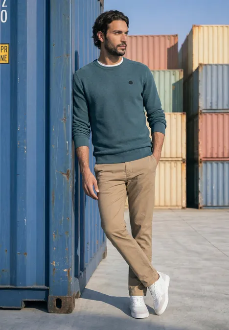 Pullover mit Rundhals und Schulterdetail cold blue Ein Mann lehnt lässig an einem blauen Frachtcontainer, umgeben von bunten Containerstapeln.