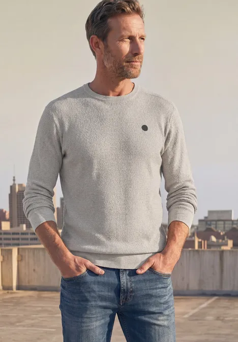 Pullover mit Rundhals und Schulterdetail bright beige melange Ein blonder Mann mit grauem Pullover und Jeans steht lässig auf einem Parkdeckdach und schaut in die Ferne.