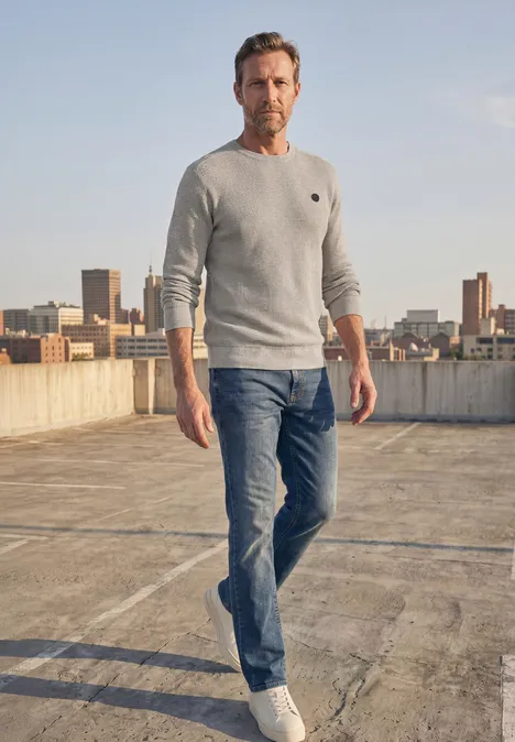 Pullover mit Rundhals und Schulterdetail bright beige melange Ein Mann in Jeans und Pullover steht auf einem Dach mit urbaner Skyline im Hintergrund.