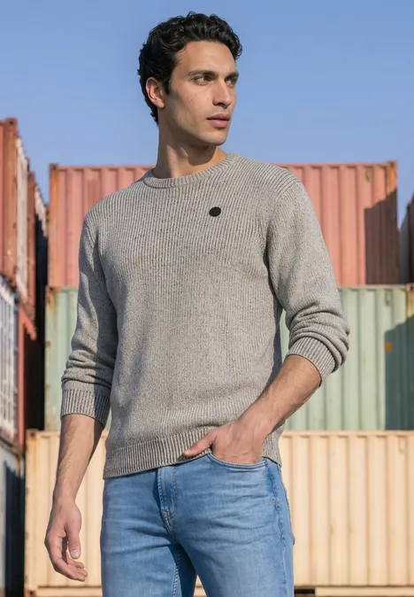 Mouliné Pullover mit Rundhals silver grey melange Ein Mann in grauem Pullover und blauen Jeans steht vor bunten Frachtcontainern im Freien.