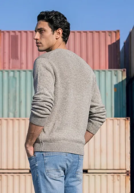 Mouliné Pullover mit Rundhals silver grey melange Ein Mann im grauen Pullover und Jeans steht vor gestapelten Containern und schaut seitlich.