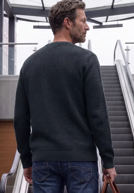 Sweter o strukturze melanżowej dark basic blue melange Mężczyzna w czarnym swetrze z torbą stoi przy ruchomych schodach.