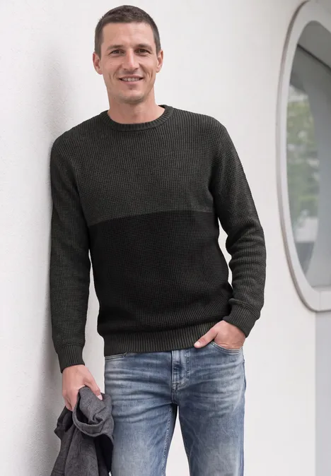 Sweter z okrągłym dekoltem i elementami w stylu mouliné anthra grey melange Mężczyzna w swetrze i dżinsach opiera się o białą ścianę, trzymając w ręku kurtkę.