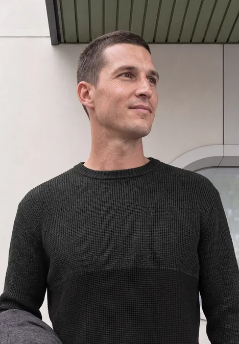Sweter z okrągłym dekoltem i elementami w stylu mouliné anthra grey melange Mężczyzna w ciemnej bluzie patrzy w bok na jasnym tle.
