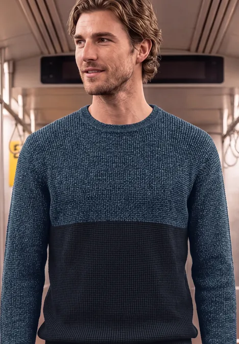 Sweter z okrągłym dekoltem i elementami w stylu mouliné dark basic blue melange Mężczyzna w dwukolorowym swetrze stoi w wagonie metra lub pociągu.