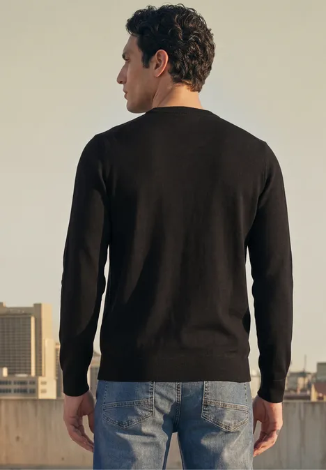 Mann steht auf einem Dach, Rückansicht, trägt schwarzen Pullover und Jeans, Stadtblick im Hintergrund.