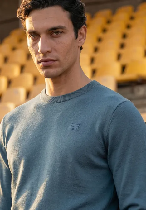 Junger Mann in einem blauen Sweatshirt vor leeren Stadiontribünen.
