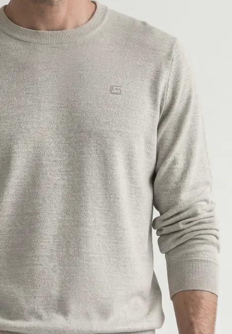 Ein Mann trägt einen hellgrauen, fein gestrickten Pullover mit Rundhalsausschnitt.