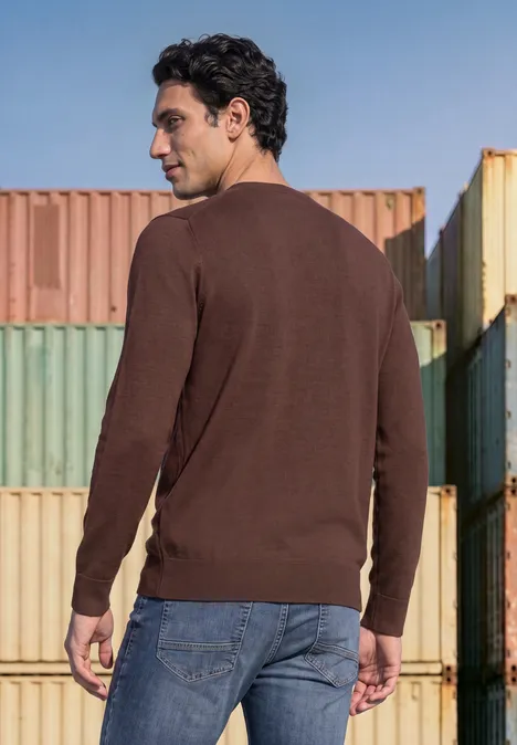 Ein Mann in braunem Pullover und Jeans steht vor bunten Containern, Blick nach oben.