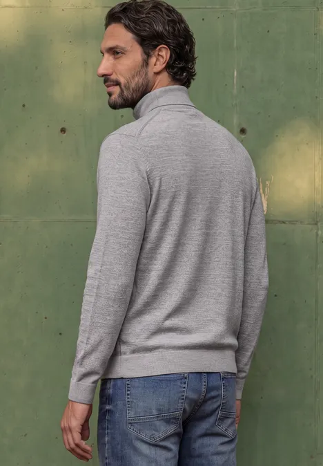 Basic sweter z golfem silver grey melange Mężczyzna od tyłu w szarym golfie i dżinsach na tle zielonej ściany.