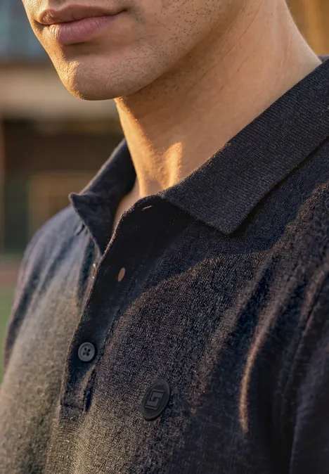 Nahaufnahme eines Mannes, der ein dunkelblaues Poloshirt mit offenem Kragen und dezentem Logo trägt.