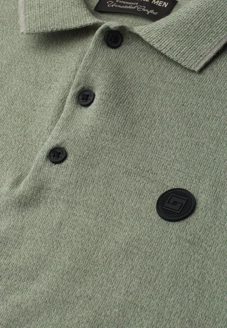 Nahaufnahme eines olivgrünen Poloshirts mit Knopfleiste, Kragen und rundem, schwarzem Logopatch.