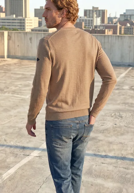 Ein Mann in braunem Pullover und Jeans steht auf einem Parkdach, Blick auf die Stadt.