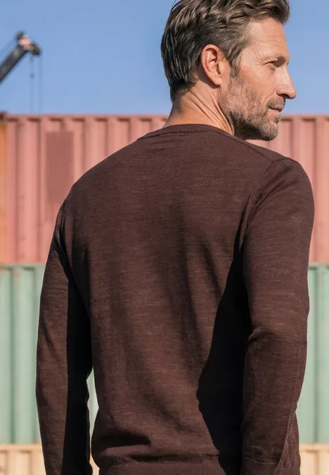Ein Mann in braunem Langarmshirt, Rückenansicht vor bunten Transportcontainern.