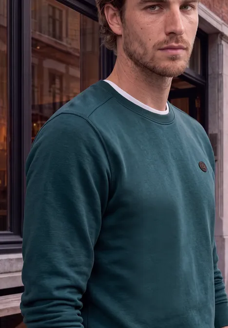 Ein Mann in grünem Sweatshirt steht vor einem historischen Gebäude.