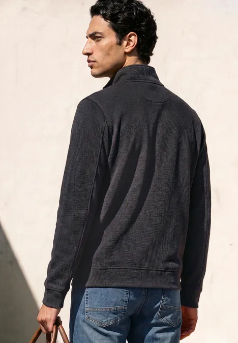 Sweatshirt à col montant et fermeture zip Black Ein Mann in dunkler Jacke steht seitlich, blickt nach links vor hellem Hintergrund.