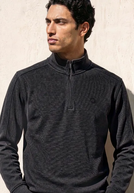 Sweatshirt à col montant et fermeture zip Black Ein Mann mit dunklem, schmal geschnittenem Zip-Pullover steht vor hellem Hintergrund.