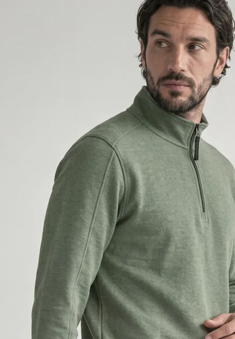 Ein Mann im grünen Pullover mit Reißverschluss schaut zur Seite.
