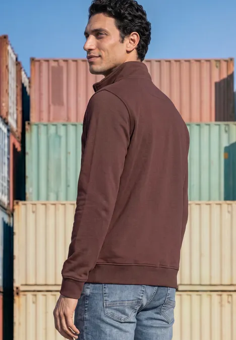 Ein Mann in brauner Sweatjacke steht seitlich vor bunten Containerwänden.
