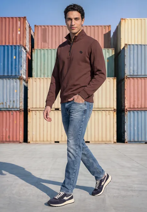 Ein Mann in braunem Pullover und Jeans läuft vor bunten Frachtcontainern.