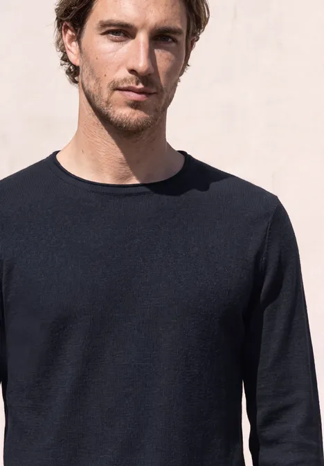 Een man met bruin haar en een zwarte trui voor een lichte achtergrond.