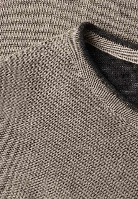 Close-up van een grijs-beige fijngebreide trui met ribbelstructuur en ronde hals.