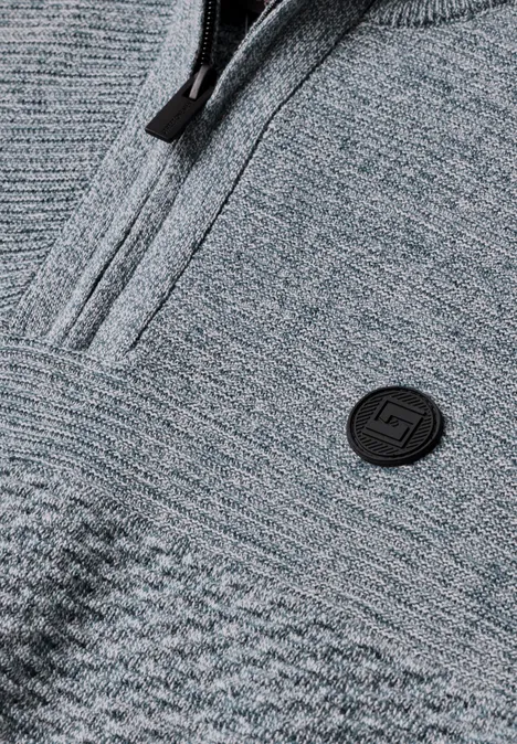 Pullover mit Troyerkragen und Struktur vintage blue Nahaufnahme eines grauen Strickpullovers mit Reißverschluss und rundem Logo auf der Brust.