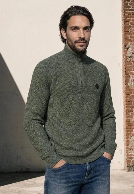 Pullover mit Troyerkragen und Struktur willow green Ein Mann trägt einen grünen Pullover mit kurzem Reißverschluss und Jeans und steht vor einer Wand.
