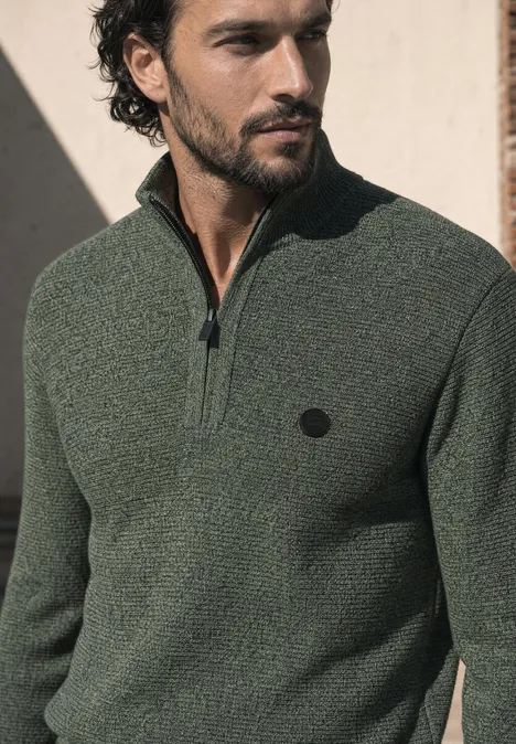 Pullover mit Troyerkragen und Struktur willow green Mann mit dunkelgrünem Strickpullover mit halbem Reißverschluss und Logo, schaut seitlich.