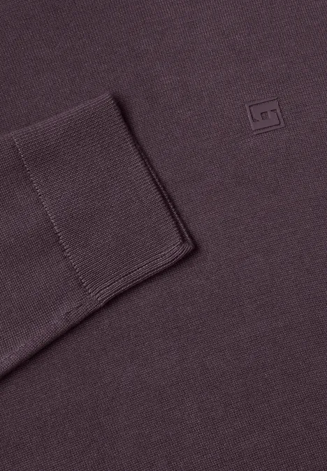 Nahaufnahme eines auberginefarbenen Strickpullovers mit Bündchen und kleinem Quadrat-Logo.