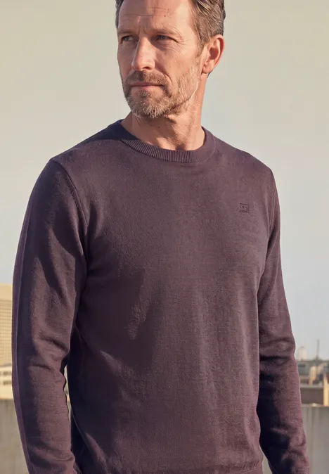 Mann mit dunkelgrauem Pullover vor neutralem Hintergrund.