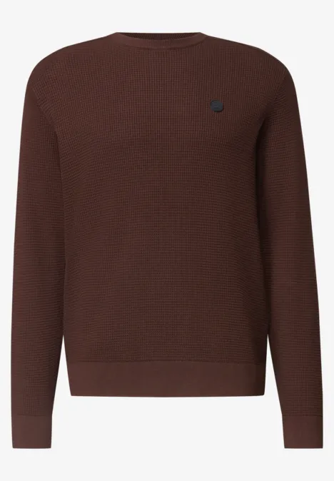 Ein schlichter, brauner Pullover mit Rundhalsausschnitt und kleinem Logo auf der Brust.