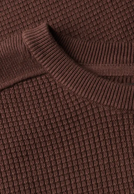 Nahaufnahme eines braunen, strukturierten Strickpullovers mit Waffelmuster.