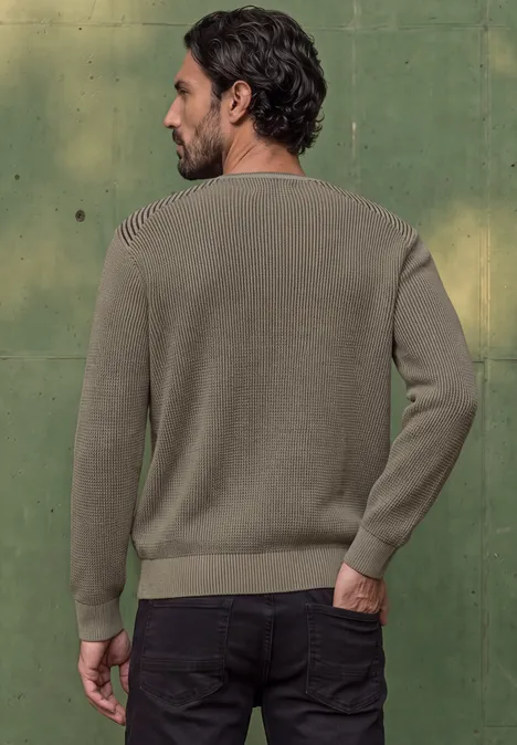 Un homme de dos en pull kaki devant un mur vert.