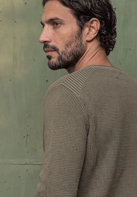 Homme en pull vert en profil, devant un fond vert.
