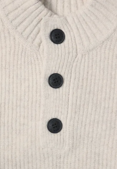 Beiger, gerippter Strickpullover mit hohem Kragen und einer Knopfleiste mit drei dunklen Knöpfen.