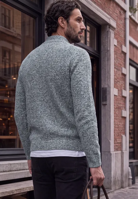 Mann in grauem Pullover und schwarzer Hose mit Ledertasche läuft durch die Stadt.