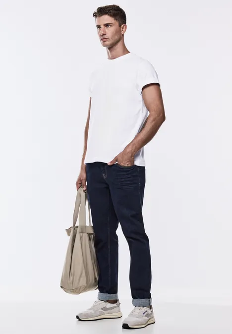 Mann in weißem T-Shirt und Jeans mit Stofftasche in der Hand.